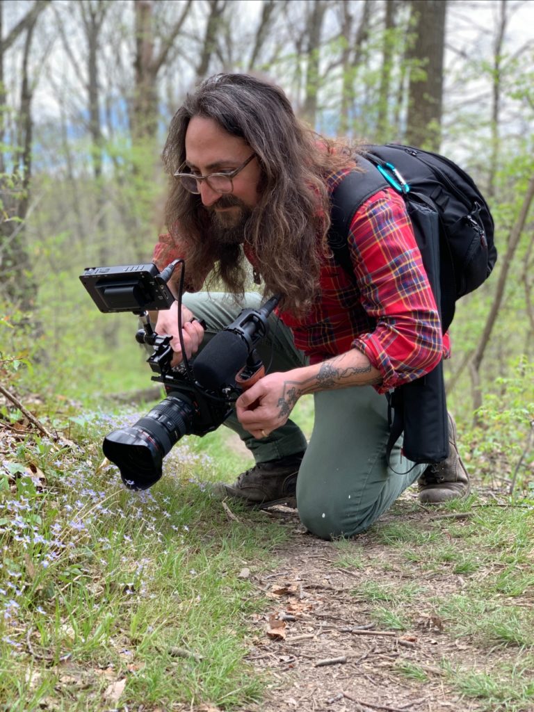 person crouched down outdoors holding a camera 