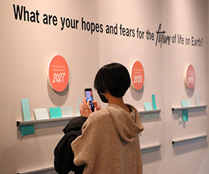 A visitor photographs a wall with text: What are your hopes and fears for the future of life on earth?